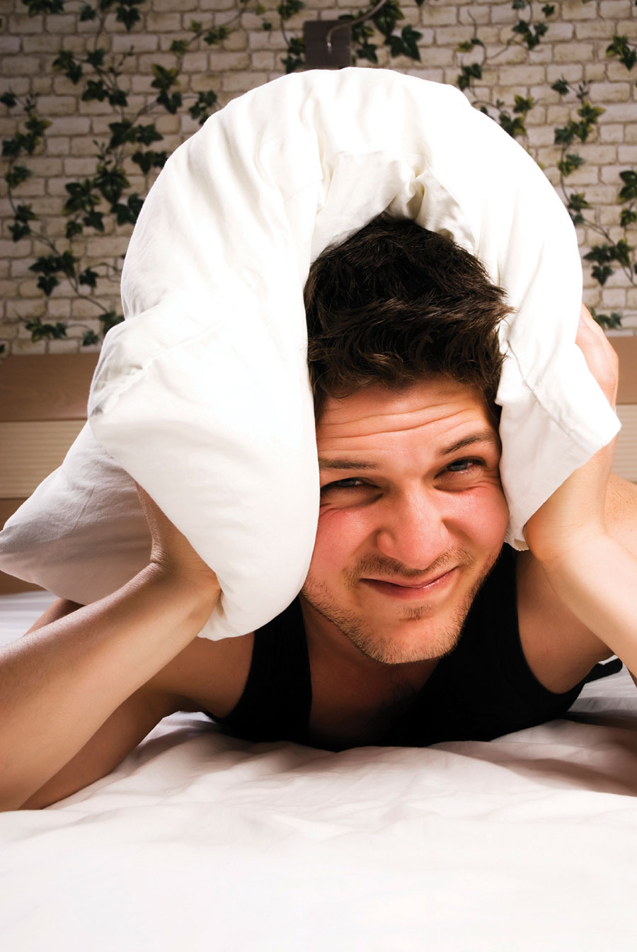 Man in bed with pillow over his head